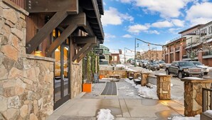 A stone building with a wooden staircase leading to a covered outdoor seating area. - Downtown Barnwood Condo. WSTR-21-00029 (Whitefish)