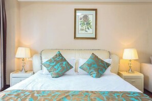 Une chambre d’hôtel avec un lit, deux lampes de chevet et une illustration botanique encadrée accrochée au mur.