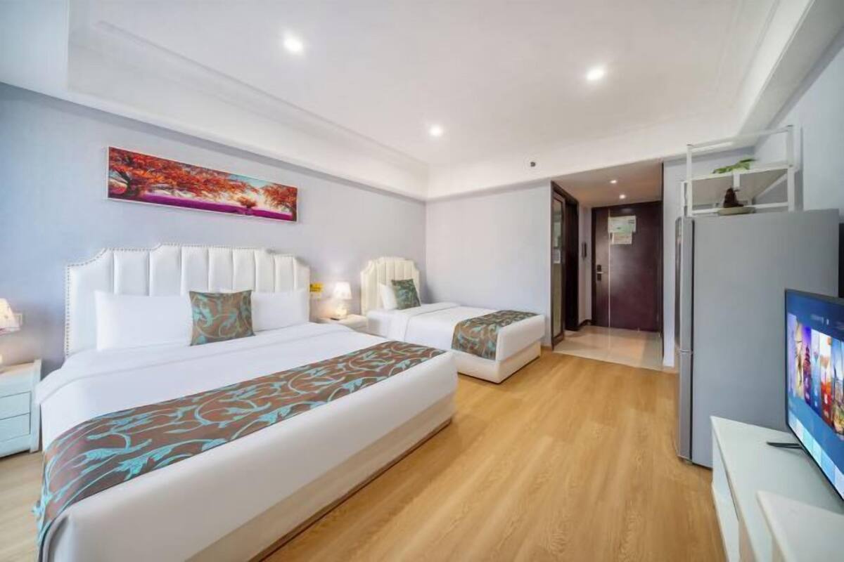 Ein Hotelzimmer mit einem großen Bett, einem kleineren Bett, einem Fernseher und einem Bild an der Wand.