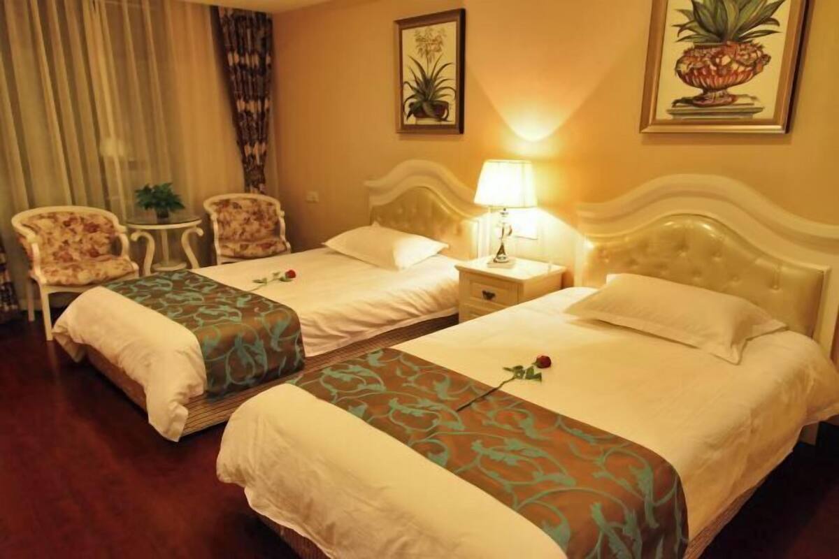Ein Hotelzimmer mit zwei Betten, einem Nachttisch, einer Lampe, einem Sessel und einem kleinen Tisch.