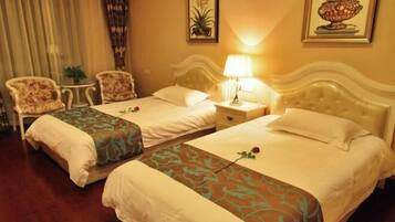 A hotel room with two beds, a nightstand, a lamp, a chair, and a small table.