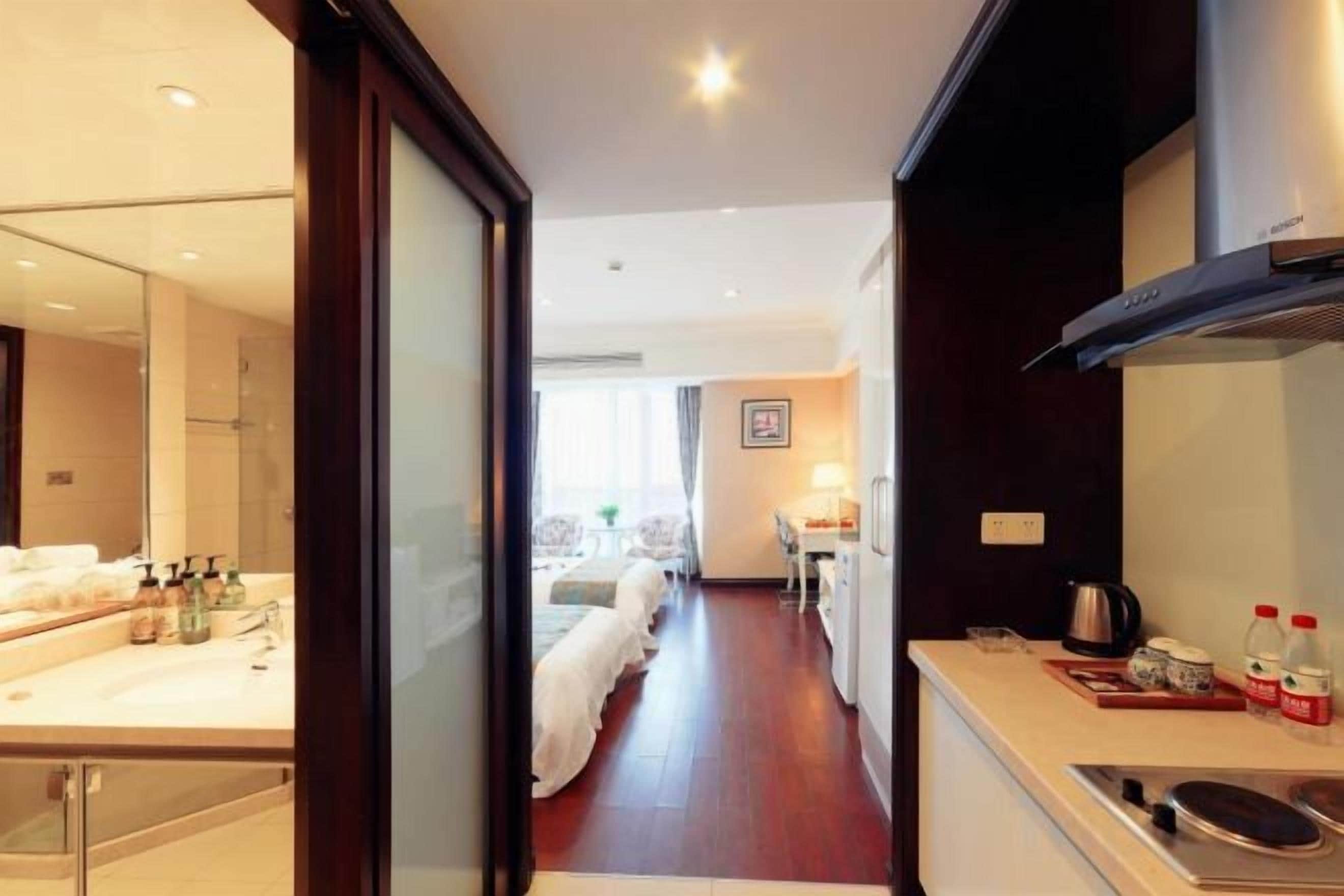 A hotel room with a large mirror, a bed, a kitchenette, and a view of the hallway.