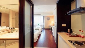 A hotel room with a large mirror, a bed, a kitchenette, and a view of the hallway. - Hangzhou Guteng Condo ApartHotel (Hangzhou)