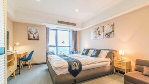 A bedroom with a bed, bedside table, lamp, chair, desk, and artwork on the walls. - Hangzhou Guteng Condo ApartHotel (Hangzhou)