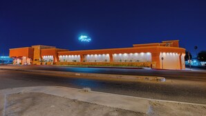 Een groot, modern gebouw met een gebogen gevel, meerdere verlichte ramen en een opvallend neonreclamebord boven de ingang.