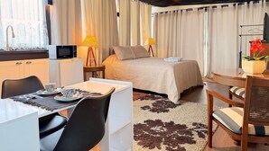 Ein modernes Hotelzimmer mit Bett, Schreibtisch, Stuhl, Esstisch und einer kleinen Küchenzeile.