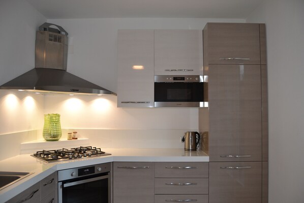 A modern kitchen with a gas stove, oven, stainless steel range hood, and built-in microwave.