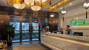 A hotel reception area with a marble counter, a receptionist, and a large glass door leading outside. - Laisili Hotel (Shanghai)