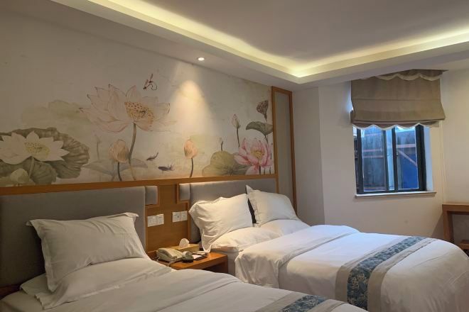 A hotel room with two beds, a floral wall mural, a bedside telephone, and a window with a curtain.