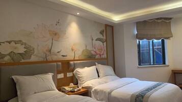 A hotel room with two beds, a floral wall mural, a bedside telephone, and a window with a curtain.