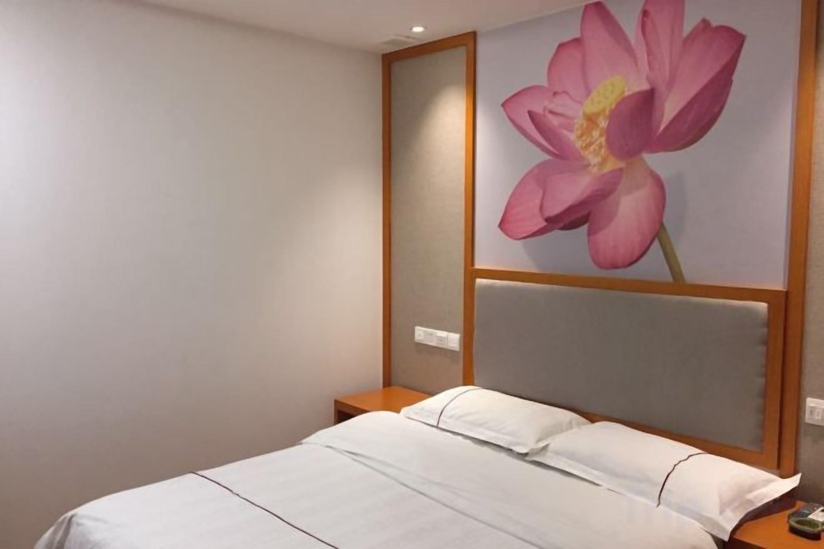 A hotel room with a bed, a nightstand, and a large floral artwork on the wall.