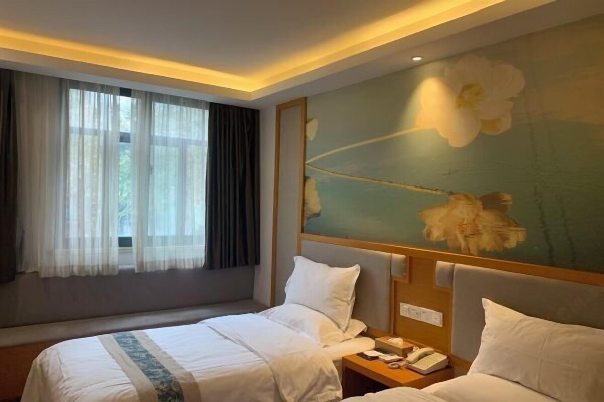 A hotel room with two beds, a large window with curtains, a wall-mounted telephone, and a floral mural.