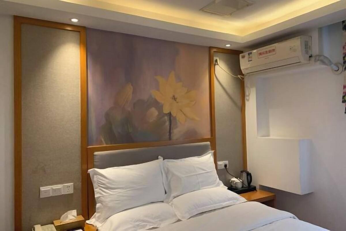 Hotellihuone, jossa on sänky, yöpöytä, taulu ja ilmastointilaite.