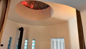 Une pièce dotée d’un plafond incurvé, d’une grande fenêtre offrant une vue sur un ciel rougeoyant et d’une porte blanche.
