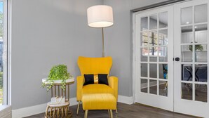 Une pièce avec un fauteuil jaune, une petite table ronde ornée d’une plante et un grand lampadaire.