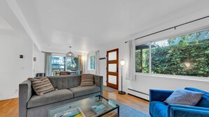 A modern living room with a grey sofa, a blue armchair, and a glass coffee table. - Mill Valley Apartment: Walking Distance to DT (Mill Valley)