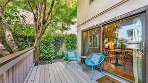 A wooden deck with two blue chairs and a table, a glass door leading inside, and a doormat with text. - Mill Valley Apartment: Walking Distance to DT (Mill Valley)