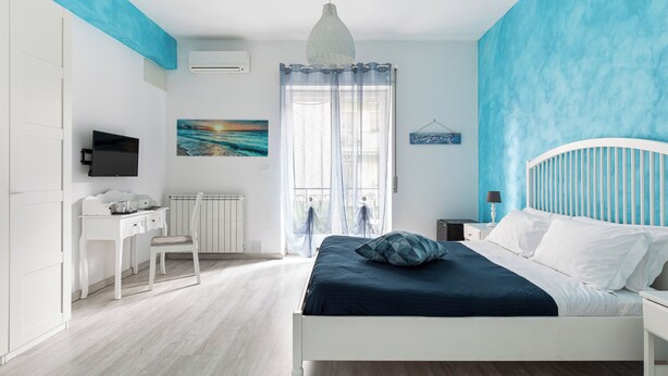 A bedroom with a bed, a desk, a chair, a TV, and a window with curtains.