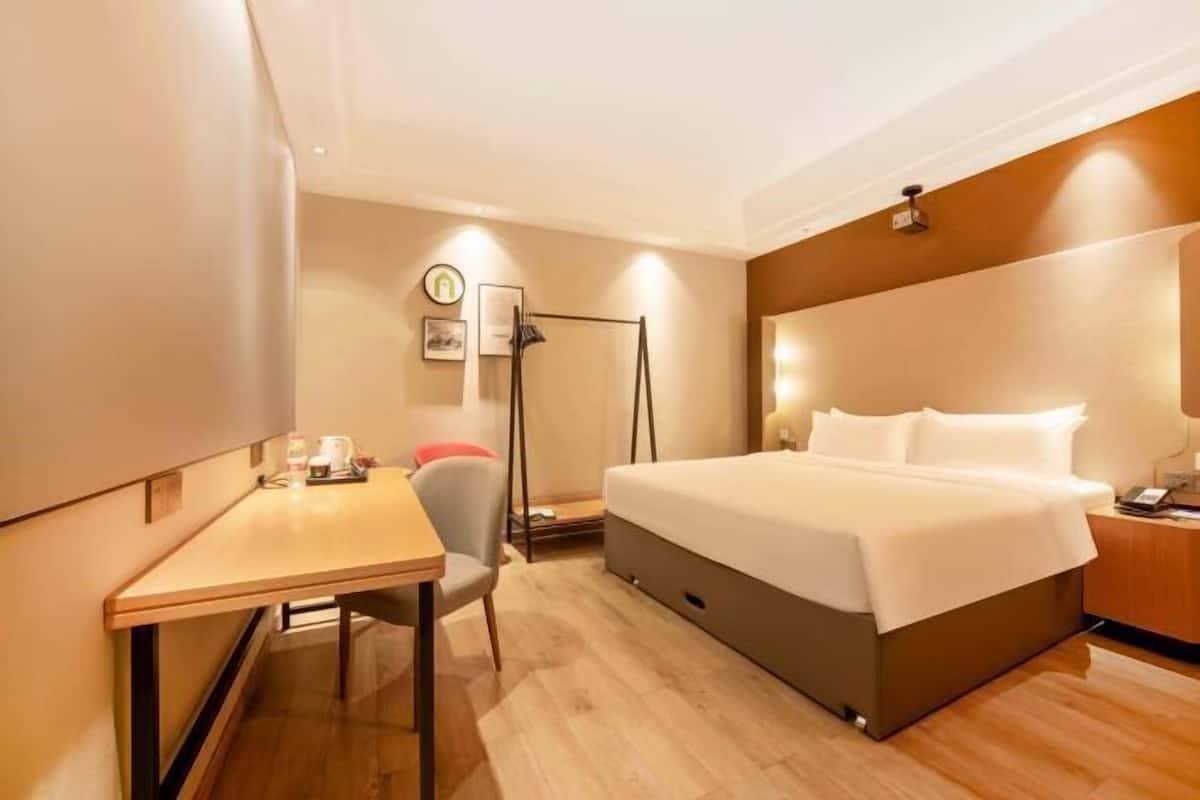 A hotel room with a bed, bedside table, chair, desk, and a floor lamp.