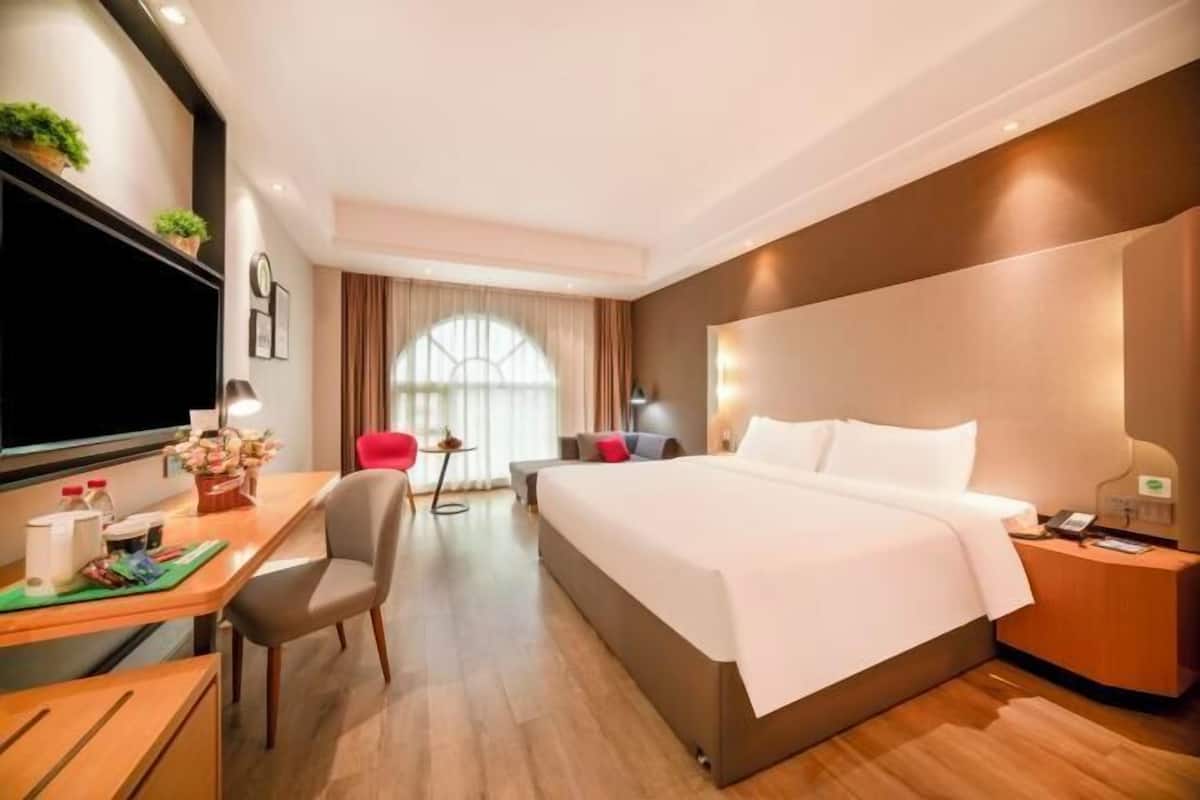 A hotel room with a bed, desk, chair, bedside table, and a TV.