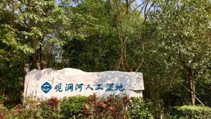 Uma placa com caracteres chineses e um logotipo, rodeada por vegetação exuberante.