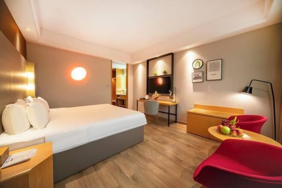 A modern hotel room with a bed, desk, chair, and a small dining area with a table and chairs.