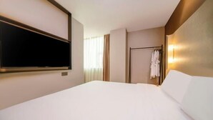 Quarto de hotel com uma cama, televisão presa à parede, guarda-roupa e espelho.