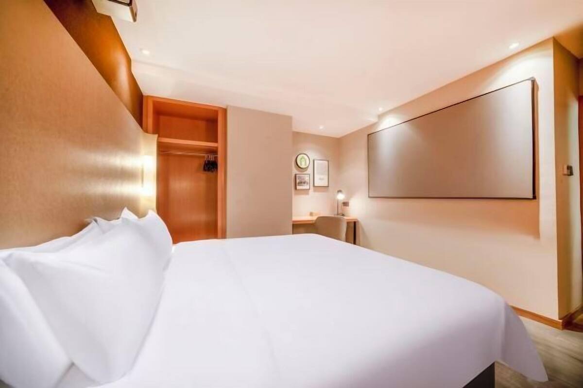 A hotel room with a large bed, a desk, and a wardrobe.