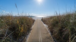 Ein Steg, der zum Strand führt, gesäumt von hohem Gras.