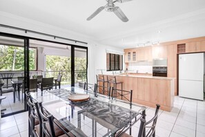 Una cocina moderna con una isla central, un comedor con mesa de vidrio y vistas a zonas verdes.