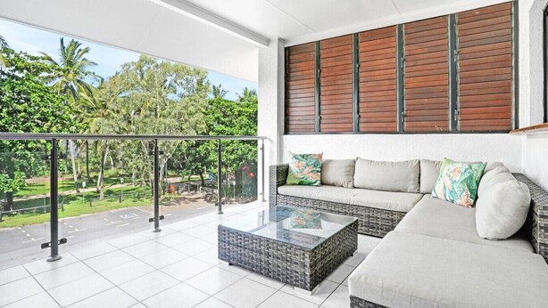 A balcony with a glass railing, a wicker sofa, and a glass coffee table. - Ocean Spray- Beachfront Retreat with Ocean Views, Jacuzzi & Pool (Yorkeys Knob)