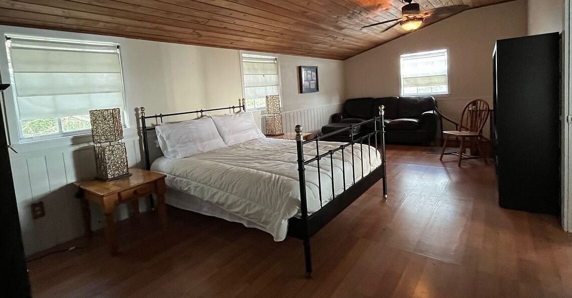 A bedroom with a single bed, a wooden bench, a black sofa, and a chair.