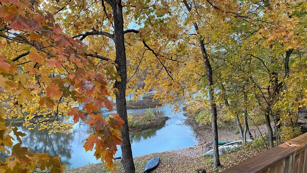 A wooden deck overlooking a calm lake with autumn foliage.