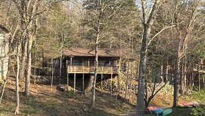 A cabin with a deck, surrounded by trees and a body of water.