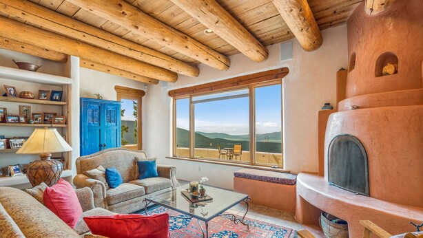 A cozy living room with a fireplace, wooden beams, a sofa, a coffee table, and a view of the mountains. - Spacious 4 bedroom with unmatched view! (Angel Fire)