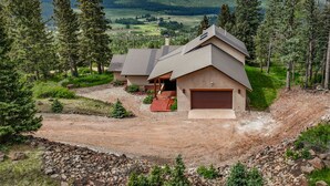 A two-story house with a large garage, surrounded by a gravel driveway and a forested area. - Spacious 4 bedroom with unmatched view! (Angel Fire)