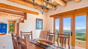 A dining area with a wooden table, chairs, and a chandelier. There is a large window with a view of the countryside. - Spacious 4 bedroom with unmatched view! (Angel Fire)