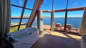 Una habitación con un ventanal grande, una bañera y una terraza de madera con vistas a un cuerpo de agua.