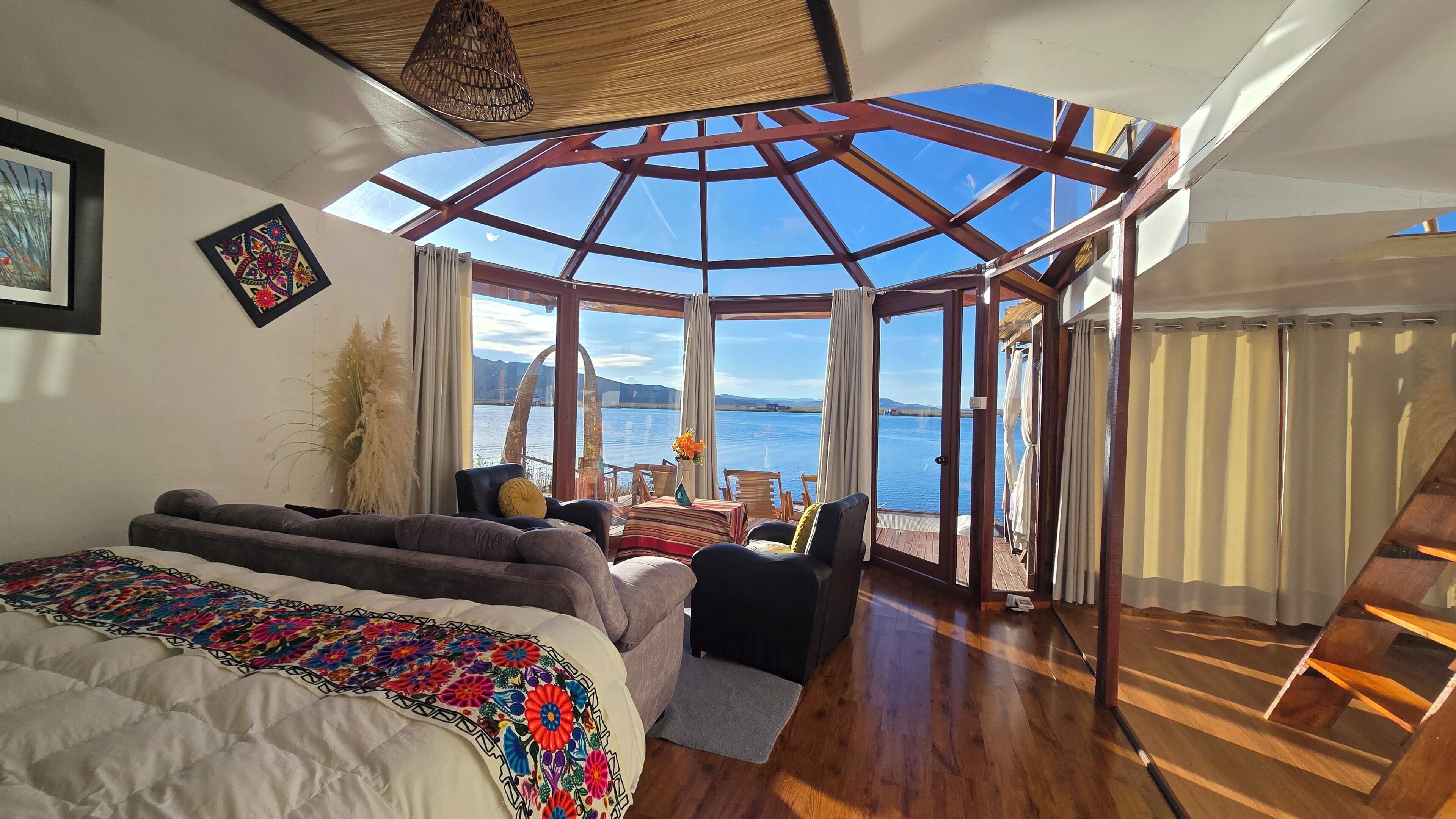 Una habitación con cama, sofá, zona de comedor con sillas, vista al agua y estructura de techo de madera.