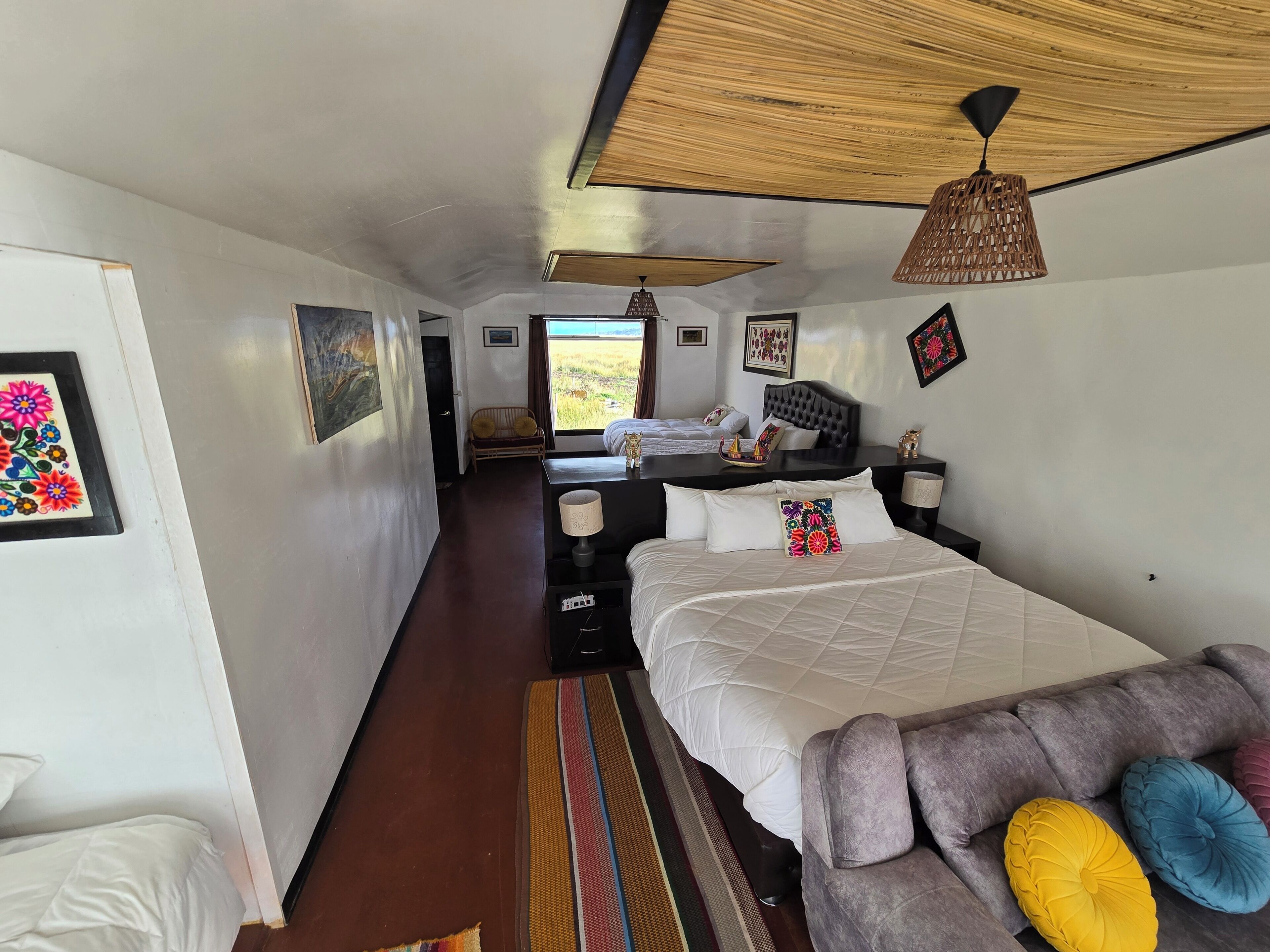 Un dormitorio con cama, sofá, mesita de noche, lámpara y vistas al exterior.