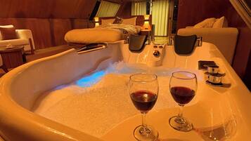 Un jacuzzi con dos copas de vino tinto, interior de madera y vista al resto de la habitación.