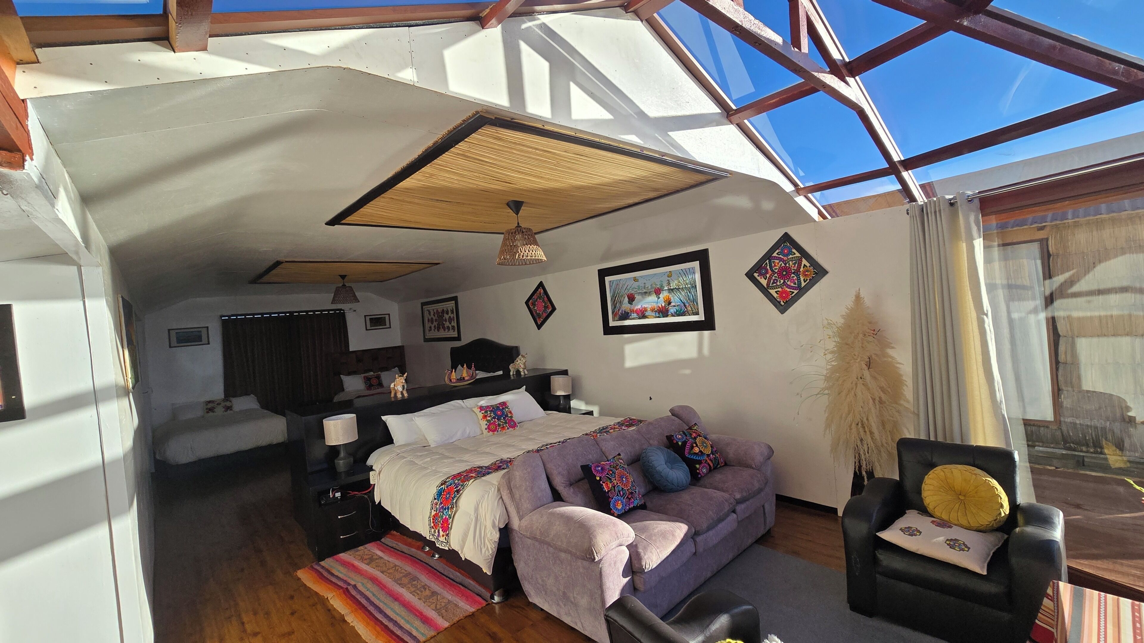 A room with a bed, a sofa, a chair, a hanging light fixture, and a wall with a framed picture.