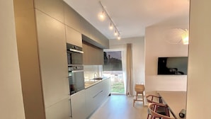 A modern kitchen with built-in appliances, a dining area with wooden chairs, and a view of the outdoors. - Modern apartment in a perfect location. Sea and old town within walking distance (Fazana)