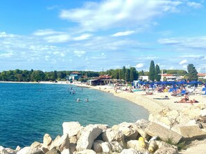 Una spiaggia con acque cristalline, un litorale roccioso e una fila di ombrelloni.