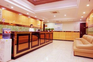 A hotel reception area with a receptionist, a reception desk, a water dispenser, and a sofa. - Zhengzhou Yaxin Hotel (Leshang Plaza) (Zhengzhou)