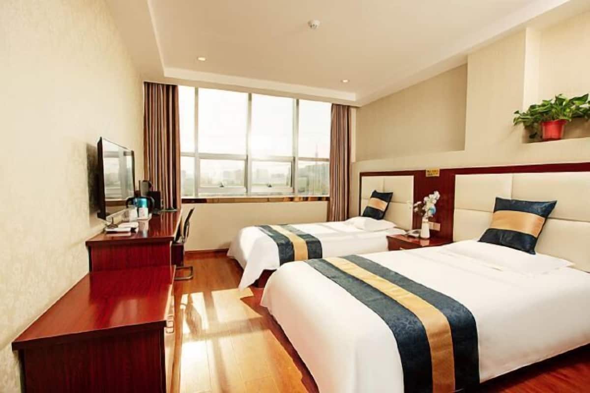 Une chambre d’hôtel avec deux lits, un bureau, une chaise, une télévision et une fenêtre avec des rideaux.