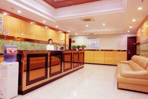 Un espace d’accueil d’hôtel comprenant un comptoir de réception en bois, un canapé et un distributeur d’eau.