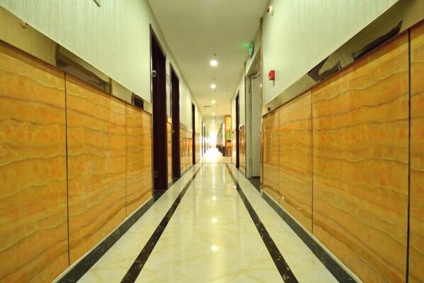 Un pasillo de hotel con piso pulido, paneles de madera en las paredes y puertas que dan a las habitaciones.