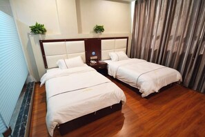 A hotel room with two beds, a wooden floor, a headboard with a control panel, and a curtain on one side.