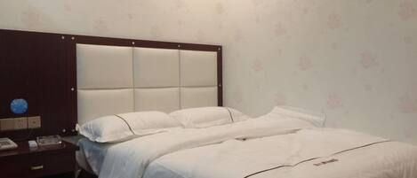 A hotel room with a large bed, a nightstand with a phone, and a wall clock.